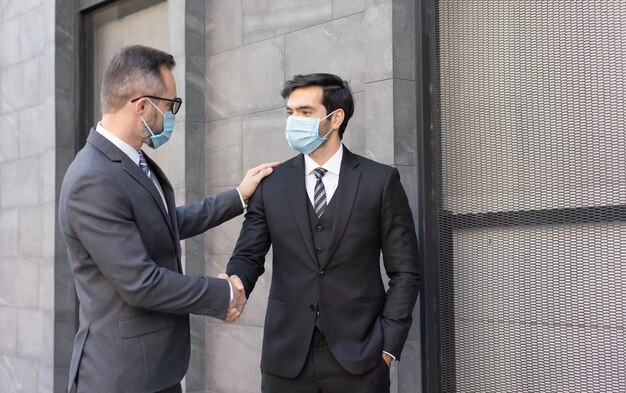 Twee blanke zakenlieden dragen een medisch masker en begroeten elkaar met een handdruk op straat in de stad