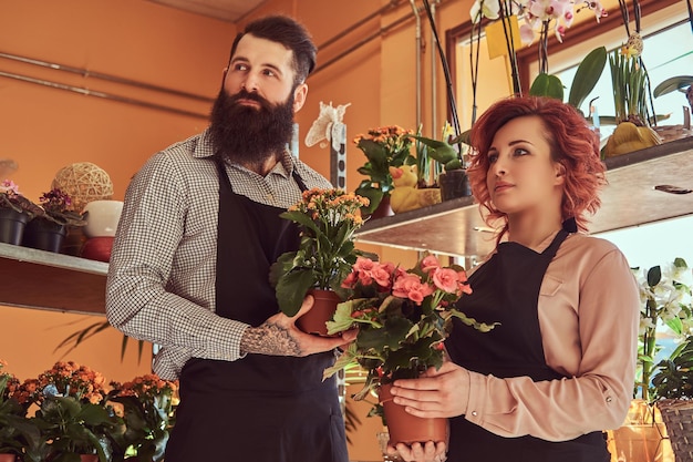 Twee bloemisten, mooie roodharige vrouw en bebaarde man met uniformen die in de bloemenwinkel werken.