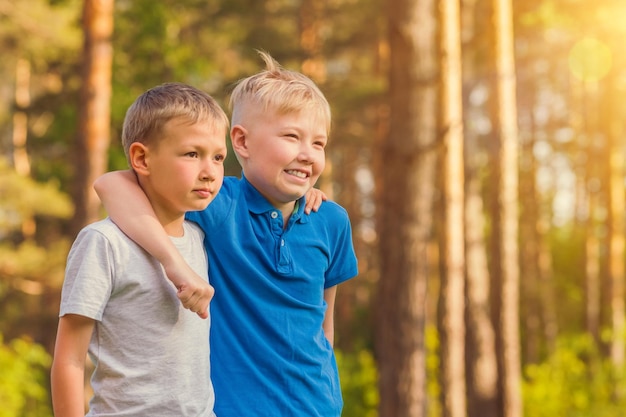 Twee blonde jongens in witte en blauwe T-shirts die elkaar omhelzen in het zonnige bos