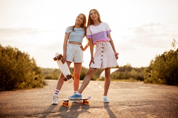 Twee blonde tieners in hipster kleding met een skateboard in een zomer park in de frisse lucht