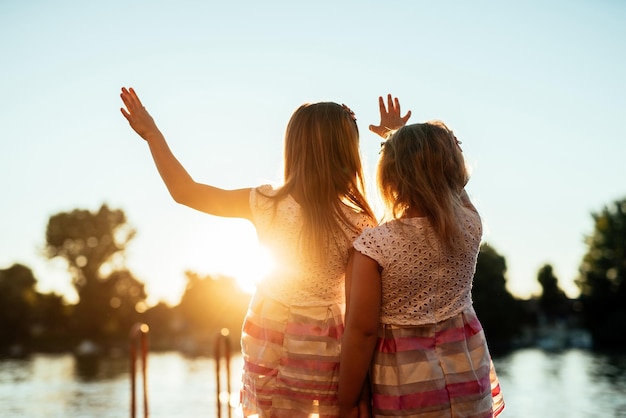 Twee blonde zussen spelen met de zon bij het meer bij zonsondergang