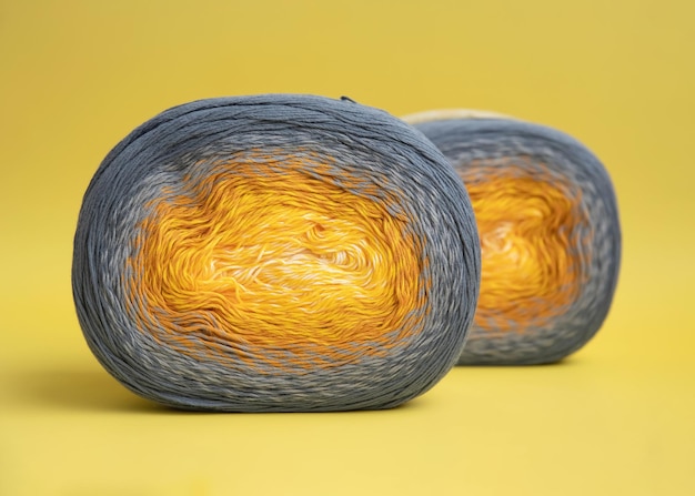 Foto twee bollen felgekleurd katoengaren met een gradiënt liggen op een gele achtergrond