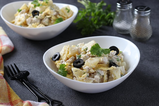 Twee borden met salade ananas, gebakken kip, omelet en zwarte olijven in witte kommen op een donkergrijze achtergrond