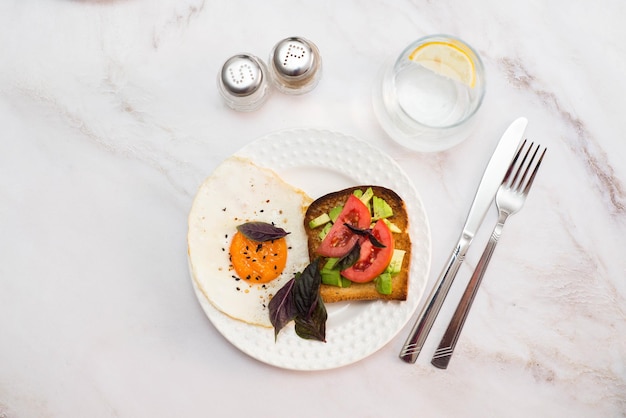 Twee borden sandwiches met avocado-tomaten gebakken eieren twee glazen water met citroen op lichte achtergrond