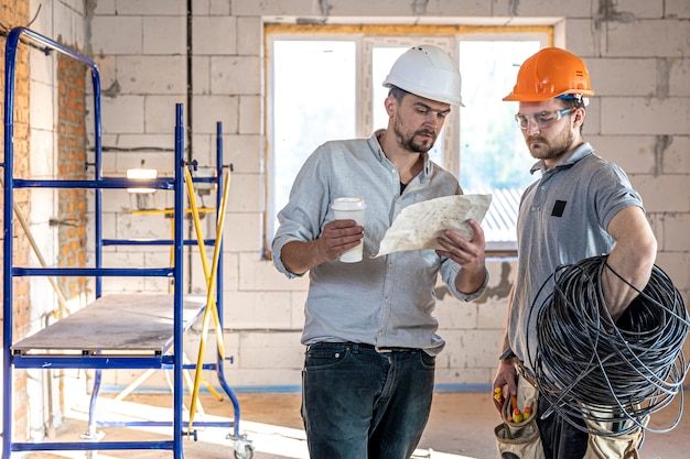 Twee bouwingenieurs praten op de bouwplaats, ingenieur legt een tekening uit aan een werknemer