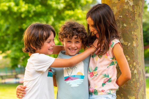 Twee broers en een zus lachend in een park naast een boom