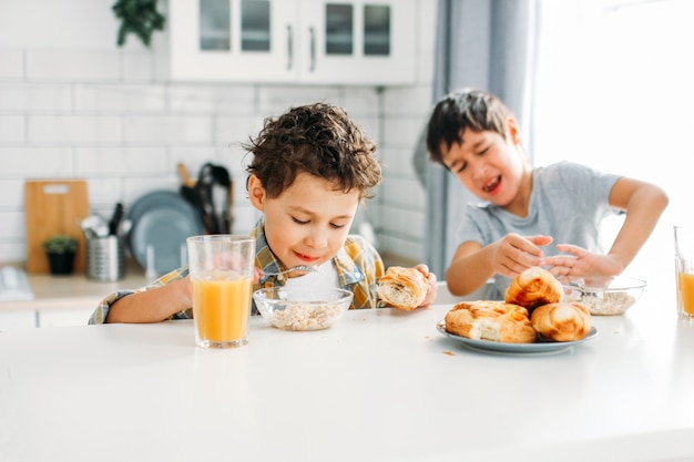 Twee broers en zussen tween jongens echte broers thuis ontbijten op lichte keuken. Kind wil niet eten