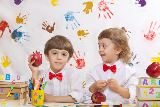 Twee broers van 7 en 4 jaar oud gekleed in witte shirts met rode strikken spelen samen.