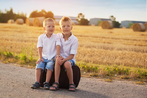 Twee broers zitten op een koffer op de weg in de zomer bij zonsondergang