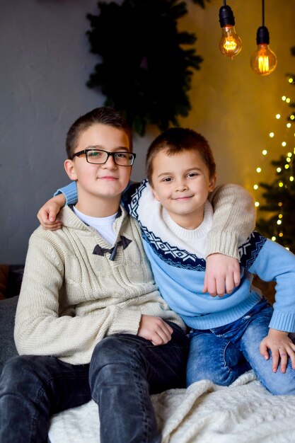 Twee broers zitten op het bed en glimlachen terwijl ze elkaar omhelzen in de versierde kerstwoonkamer