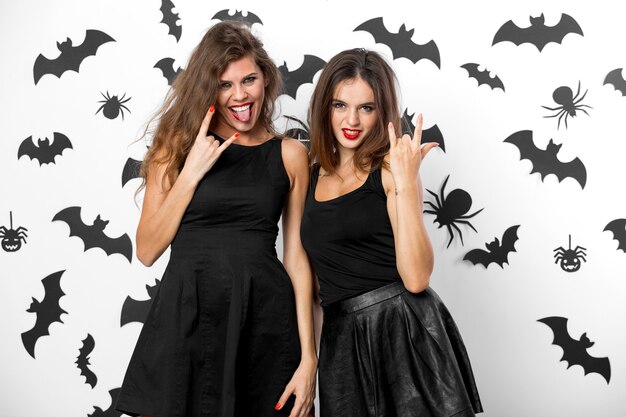 Twee brunette meisjes gekleed in zwarte jurken grimassen op de achtergrond van de muur met vleermuizen. Halloween feest. .