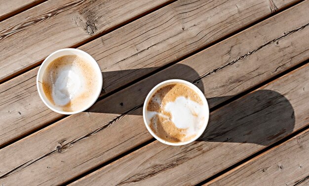 Twee cappuccino in beige papieren bekers op houten gestreepte tafel buiten koffie drinken en vrienden ontmoeten