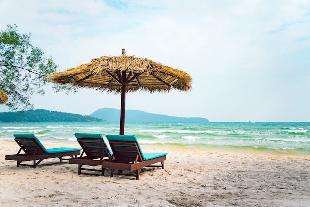 Twee chaise longues onder een stroparaplu op een strand dichtbij de zee. Tropische achtergrond. Kust van het eiland Koh Rong Samloem, Cambodja.