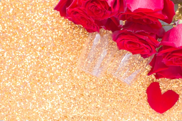 Twee champagneglazen en een rood boeket rozen liggen in de bovenhoek op een heldere gouden achtergron...