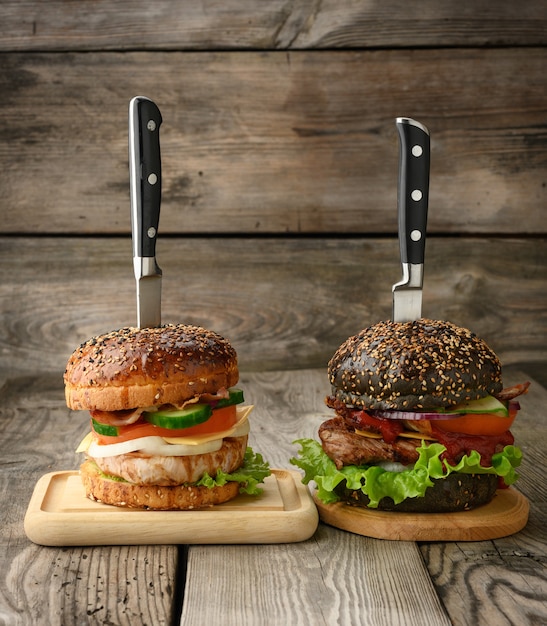 Twee cheeseburgers met groenten en vlees biefstuk op een houten bord, een sandwich wordt doorboord met een mes