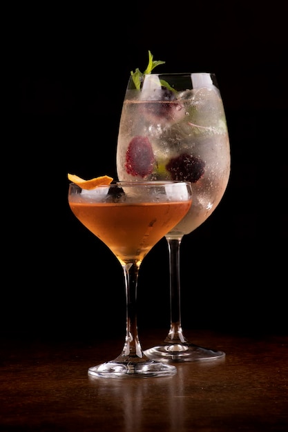 Twee cocktailglazen een martini en een witte wijn met ijs en bessen en whisky gegarneerd met sinaasappelschil