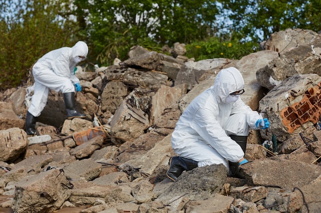 Twee collega's in beschermende pakken die kolven vasthouden en buiten op het platteland monsters nemen