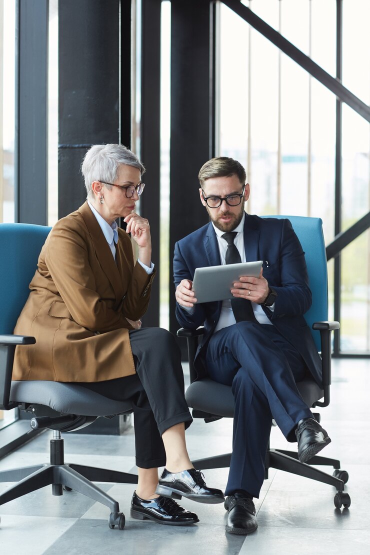 Twee collega's zitten op stoelen en met behulp van digitale tablet in hun werk zijn ze in het moderne kantoorgebouw