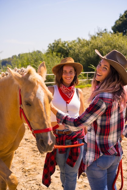 Twee cowgirl-vrouwen die een paard strelen tijdens een paardrijtocht, met Zuid-Amerikaanse outfits, de twee jonge vrouwen poseren