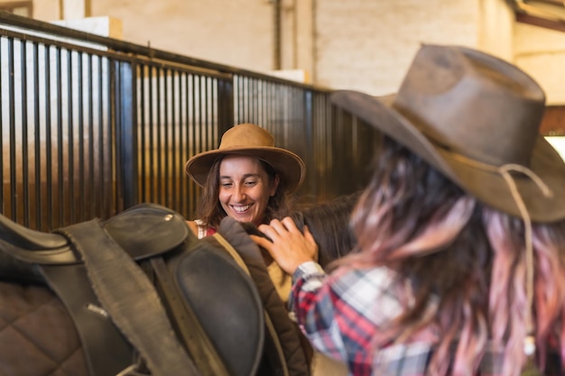 Twee cowgirl-vrouwen die zich voorbereiden om op een paard te rijden in een stal, hoeden en spijkerbroeken in het zuiden van de VS, verticale foto