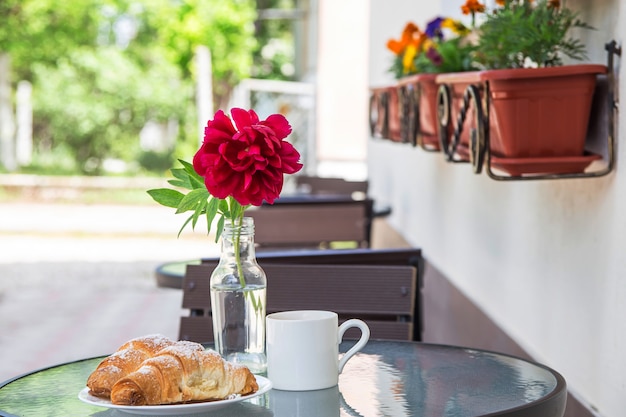 Twee croissants op een bord naast een kopje cappuccino op een straat tafel