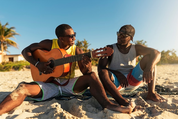 Twee Cubaanse vrienden hebben plezier op het strand met zijn gitaar. Vriendschapsconcept.