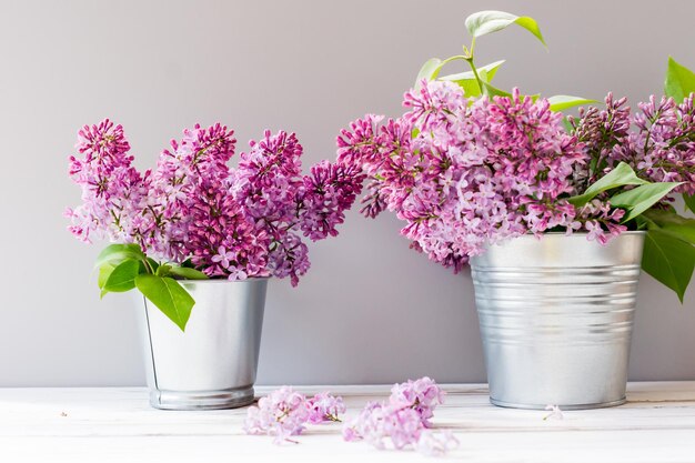 Twee decoratieve ijzeren emmers met takken van paars lila op een witte houten tafel. decoratie van een landhuis.