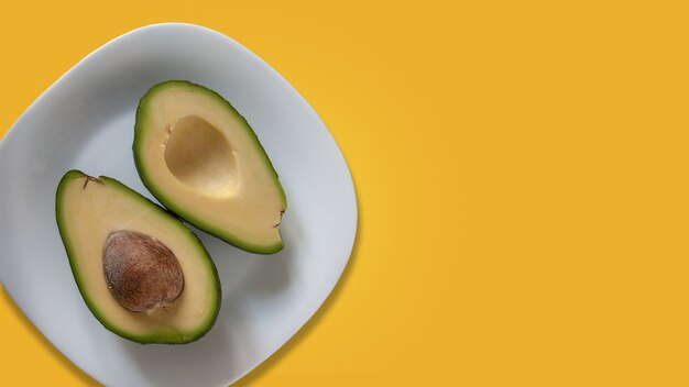 Twee delen van avocado op witte plaat. Geïsoleerd op geel.