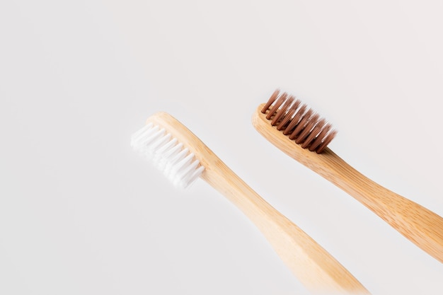 Twee diagonale houten tandenborstels, één met witte haren en de andere bruin op een lichte achtergrond