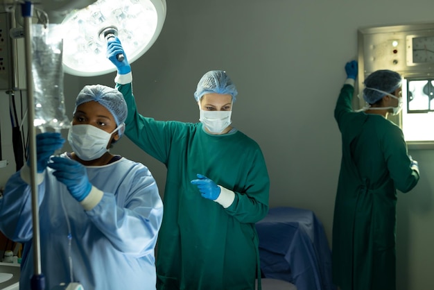 Foto twee diverse vrouwelijke chirurgische technici die tijdens de operatie het licht en de infuuszak in de operatiekamer aanpassen. ziekenhuis-, medische en gezondheidszorgdiensten.