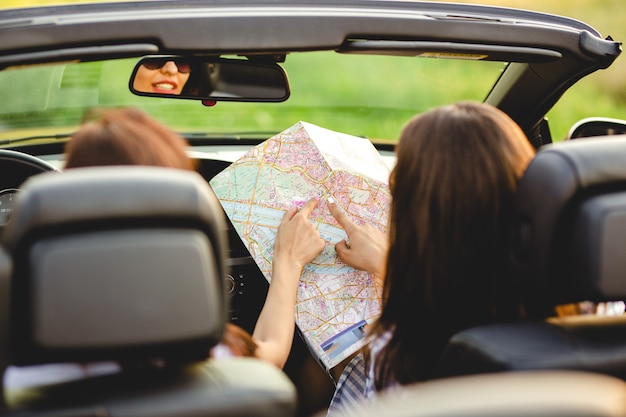 Twee donkerharige vrouwen zitten in een zwarte cabriolet en verkennen de kaart. .