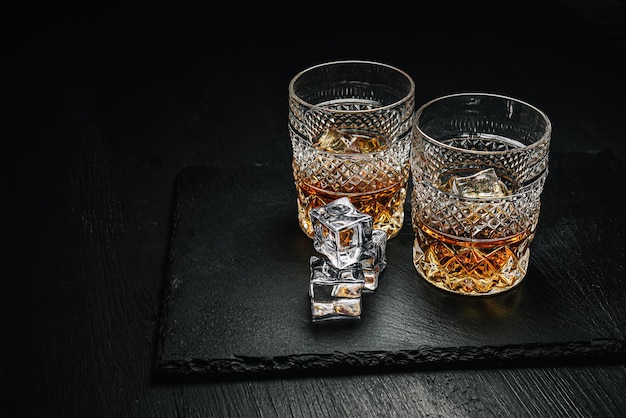 Twee dure glazen whisky met ijs op een zwart stenen dienblad