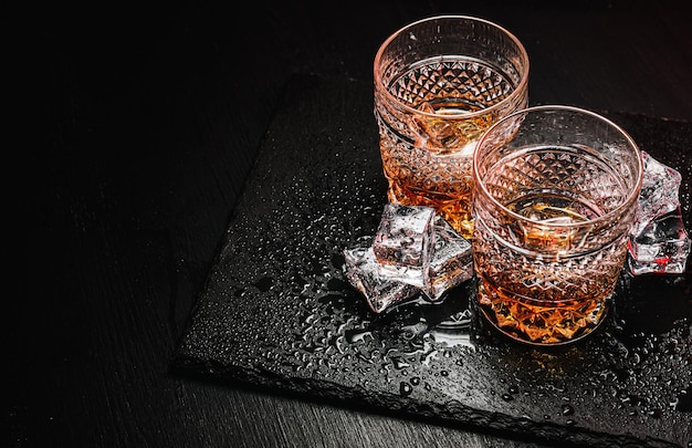 Twee dure glazen whisky met ijs op een zwart stenen dienblad