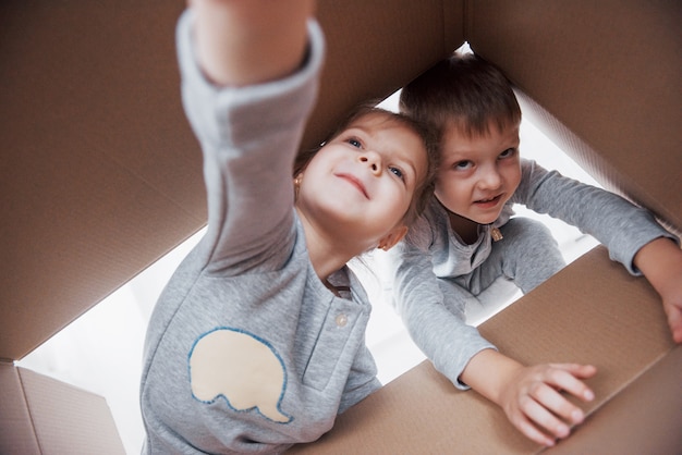 Twee een klein kinderjongen en -meisje die een kartonnen doos openen en er middenin klimmen. kinderen hebben plezier