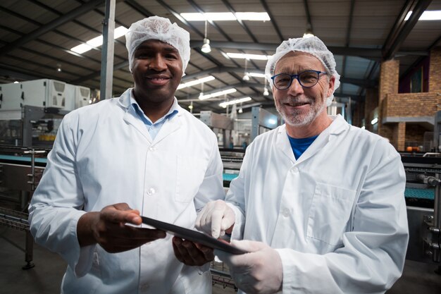 Twee fabrieksingenieurs die met digitale tablet in de drankenproductie-installatie glimlachen