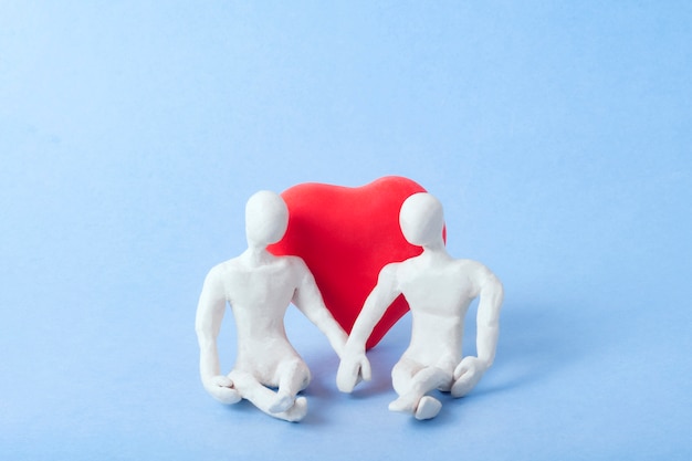 Twee figuren van witte plasticine zitten hand in hand, leunend op een groot rood hart.