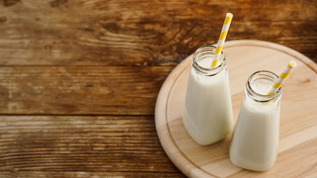 Twee flessen biologische rustieke melk op houten tafel met gele papieren rietjes. Kopieer ruimte