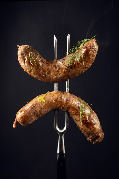 Twee gebakken rundvleesworsten op een vork Het concept van een heerlijke lunch voor een hotel op een zwarte achtergrond