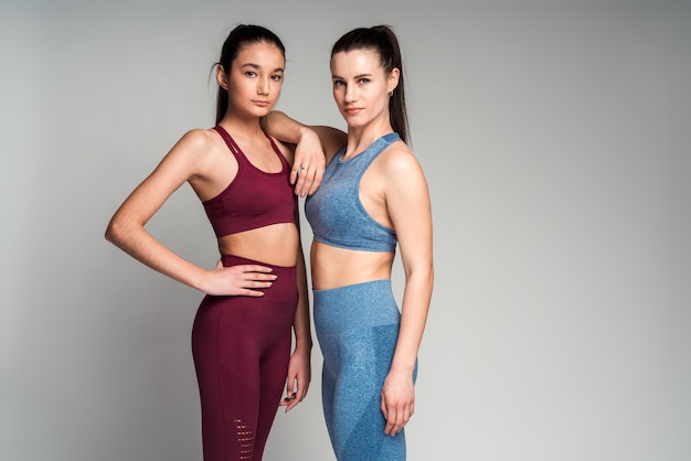 Twee geconcentreerde diverse vrouwen gekleed in sportkleding die zich aan elkaar hechten terwijl ze binnen tegen een witte achtergrond staan. mensen, sporten en sportconcept