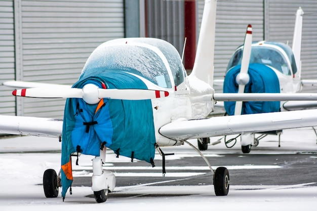 Foto twee gehulde kleine sportvliegtuigen naast de hangars