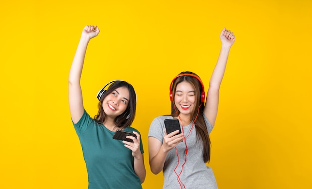 Twee geluk Aziatische glimlachende jonge vrouw die een draadloze hoofdtelefoon draagt om naar muziek te luisteren