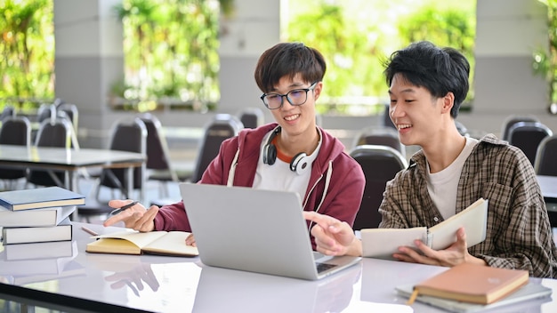 Twee gelukkige Aziatische mannelijke studenten werken samen aan hun schoolwerk