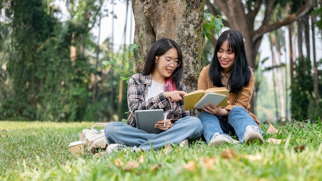 Foto twee gelukkige aziatische studenten zitten onder de boom en studeren samen.