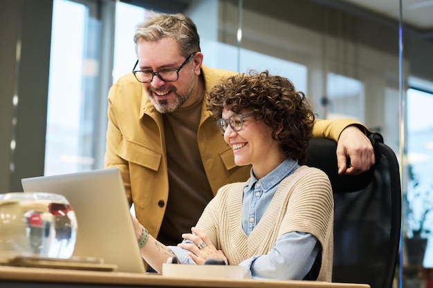 Twee gelukkige collega's bespreken online gegevens op het laptopscherm