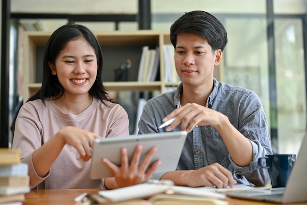 Twee gelukkige jonge Aziatische studenten kijken samen naar een tabletscherm terwijl ze discussiëren