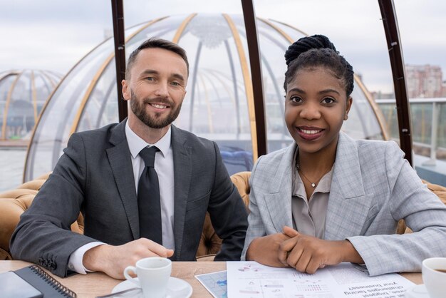 Twee gelukkige jonge interculturele economen zitten aan tafel in café