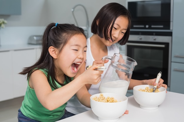 Twee gelukkige jonge meisjes die graangewassen in keuken eten