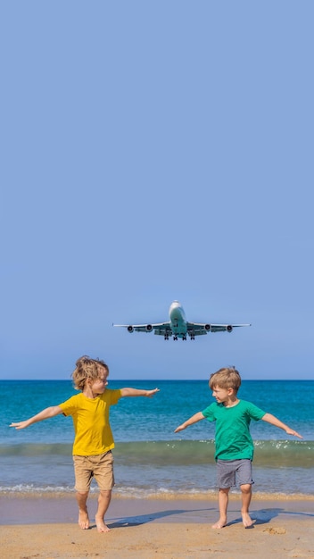 Twee gelukkige jongens hebben plezier op het strand en kijken naar de landende vliegtuigen die met kinderen in een vliegtuig reizen