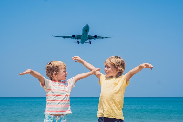 Twee gelukkige jongens op het strand en een landend vliegtuig. Reizen met kinderen concept.