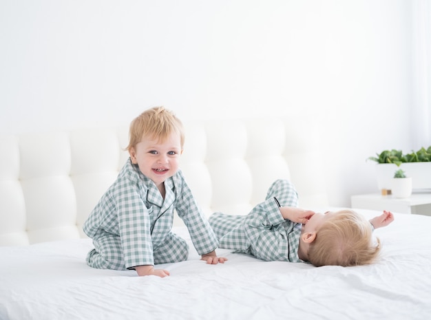 Twee gelukkige jongensbroers op wit bed in pyjama die samen pret hebben